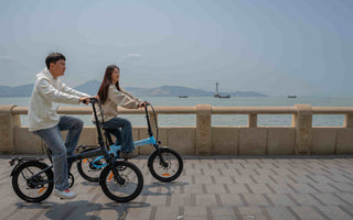 A folding electric bike riding along a steep scenic road in the Lake District with hills and lakes in the background.