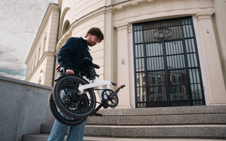 ADO Air 20 Ultra 2026 folding electric bike carried upstairs in an urban setting, lightweight folding ebike compared with standard e-bikes for UK city commuting and compact storage
