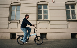 Urban commuter riding a folding electric bike with GPS navigation in a city environment, focusing on efficient battery usage