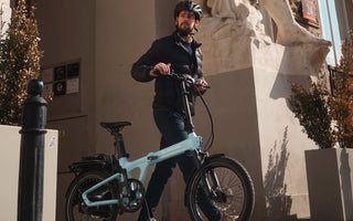 A rider commuting in the UK on a folding electric bike in an urban street environment.