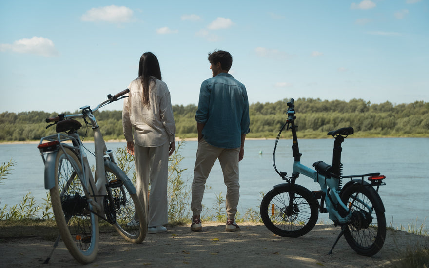 A couple looking out over a river with a cream-coloured ADO Air 28 Ultra hybrid city e-bike parked on the riverbank in the UK.