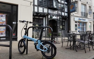 A compact folding electric bike being carried onto a London train platform, demonstrating portability for urban commuting.